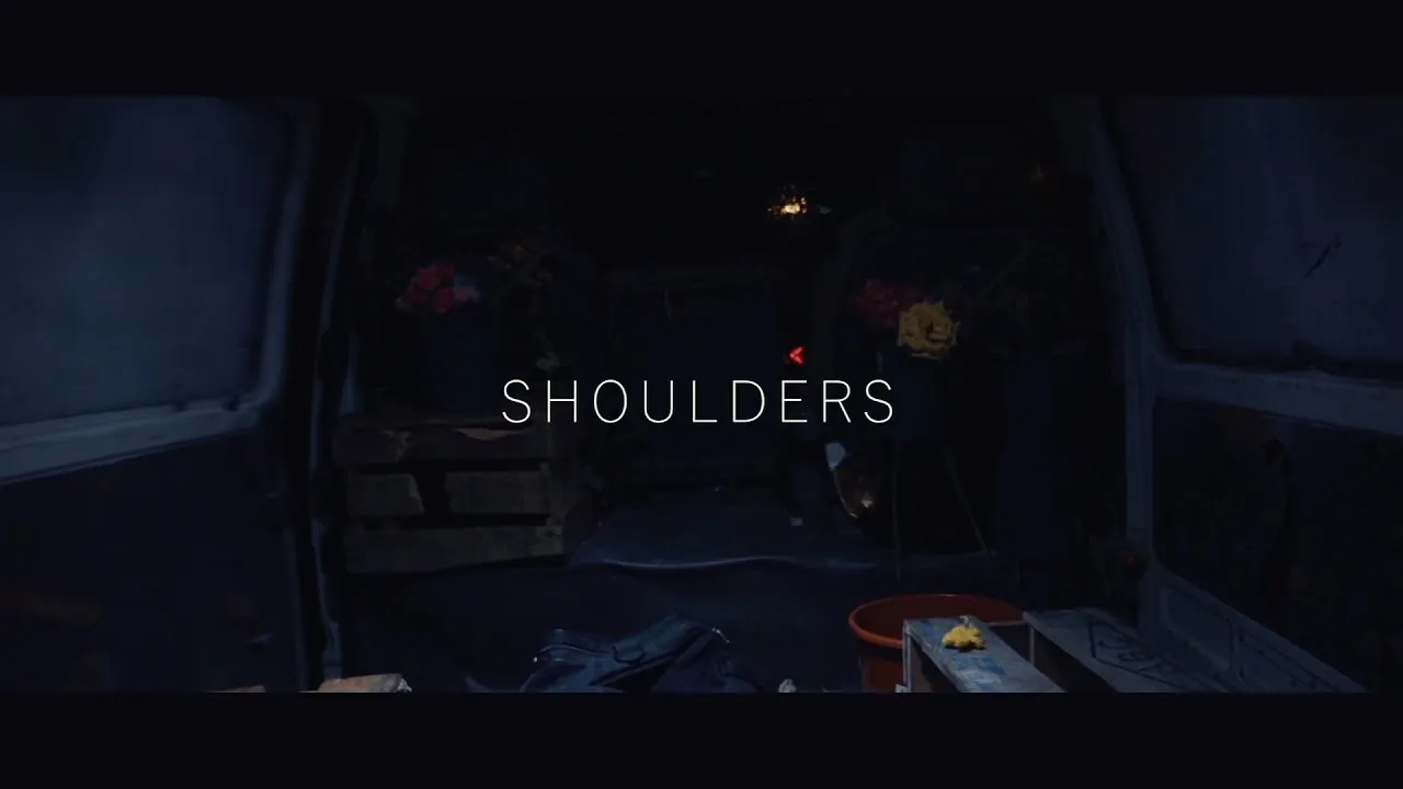 Shoulders title card over the dim interior of a van